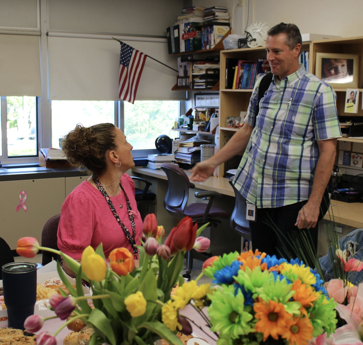 Surrounded by congratulatory flowers, Ms. Kaspar is congratulated by colleague Mr. Colvin.